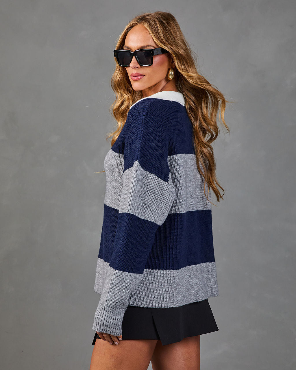 Woman wearing navy and gray striped knit sweater with white collar, black mini skirt, and oversized sunglasses