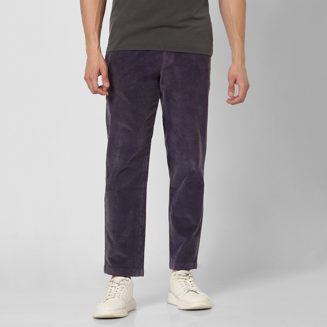 A person wears dark grey tee, white sneakers, and Corduroy Easy Pant in soft purple cotton, standing against a light background. Image cropped at the shoulders—perfect style inspiration for your fall and winter wardrobe.
