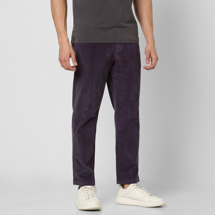 A person wears dark purple Corduroy Easy Pant, a dark gray t-shirt, and white sneakers against a plain light gray background—showing only their body from shoulders down for autumn and winter outfit inspiration.