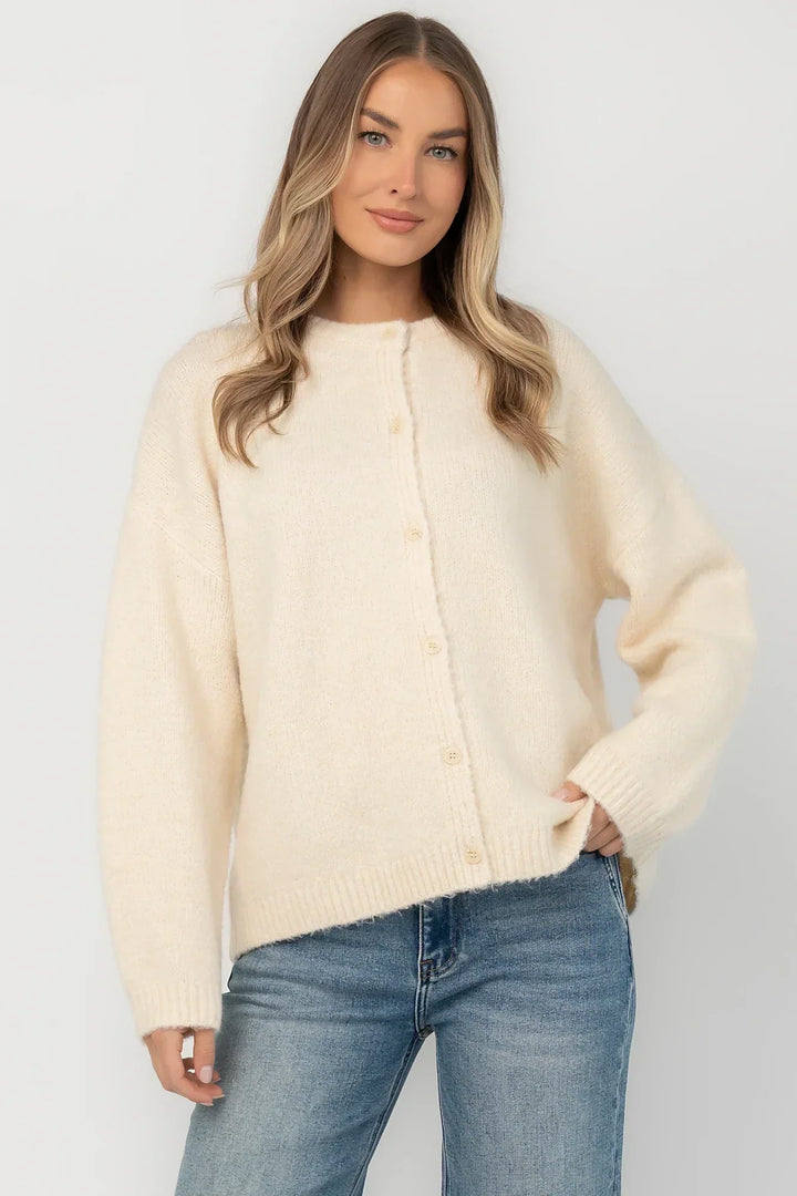 Cream fuzzy knit cardigan with a round neckline, button-front closure, long sleeves, dropped shoulders, and a relaxed fit.