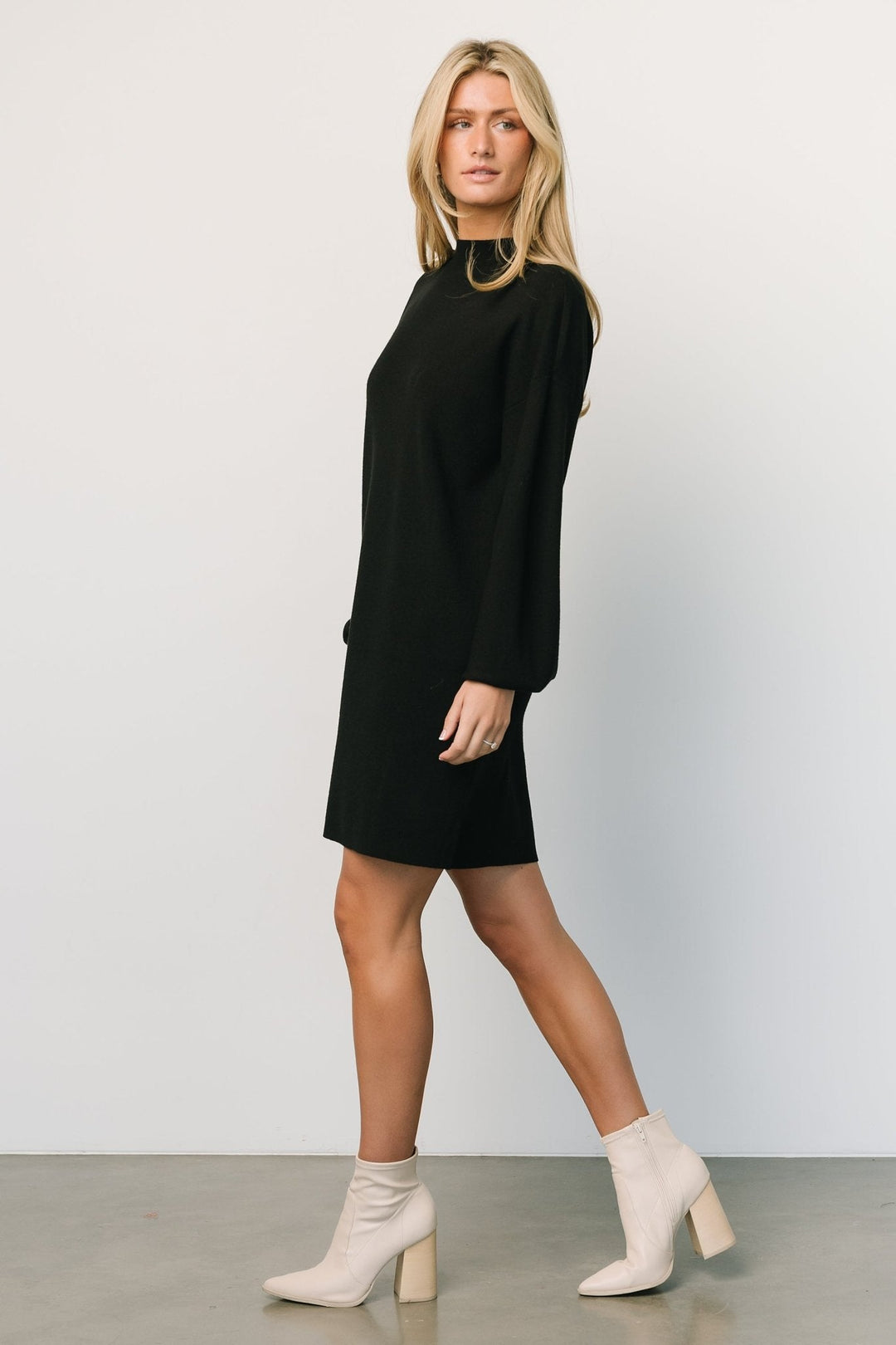 Back view of the short black sweater dress on a model, displaying clean straight silhouette and short length suitable for layering.